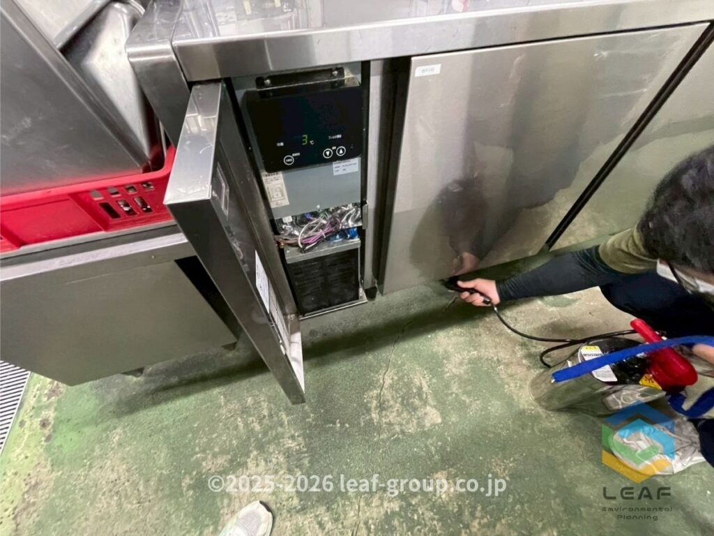 尼崎市の中華料理店厨房で冷蔵庫下へ薬剤散布を行うチャバネゴキブリ駆除作業